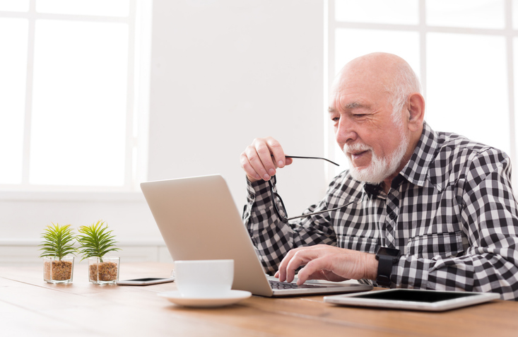 Senior man studying a laptop while holding glasses